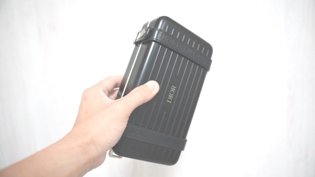 DIOR × RIMOWAのパーソナルクラッチバッグを手に持つ