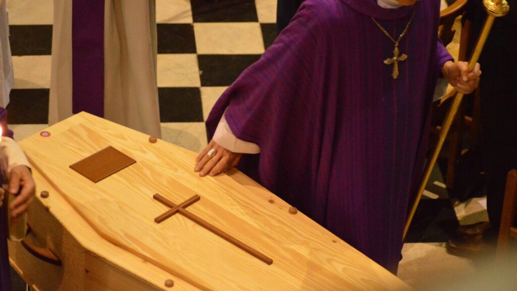 棺桶に手を添える牧師